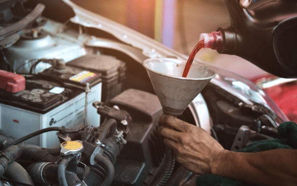 Person pouring red fluid into car engine using a funnel.