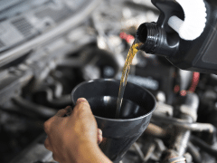 Close-up of a person's hand pouring motor oil from a bottle into a black funnel under a car's hood.