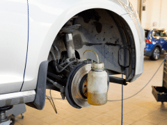 A car with the wheel removed is lifted on a jack, showing the brake fluid being drained into a container.