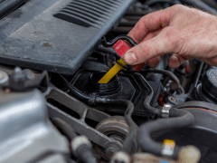 A hand holding a yellow oil dipstick near a car engine, checking the oil level.