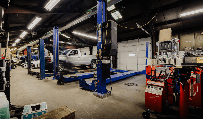 An auto repair shop with a car lifted on a blue hydraulic lift, surrounded by various tools and equipment.