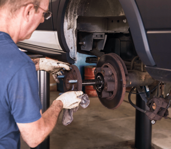 Mechanic with gloves on working on a vehicle's brake system in a repair shop.