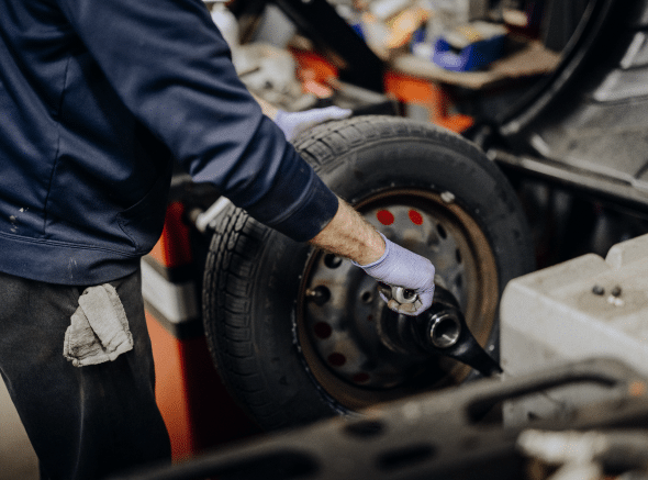 Person with purple gloves using a wrench to work on a tire in a repair shop.