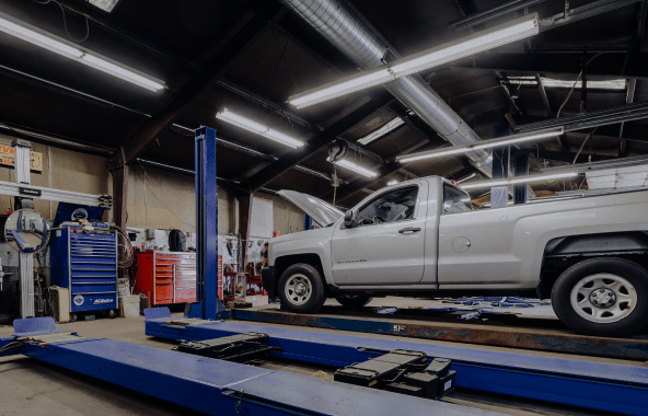 A white pickup truck on a lift in a well-lit automotive repair shop.