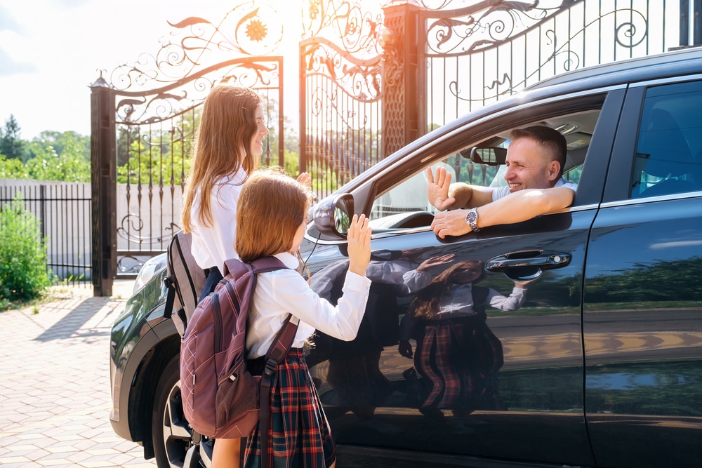 Back-to-school car preparation in Chicopee, MA, by E&G Automotive. A father in his car waves goodbye to his children as they head off to school, symbolizing the importance of a well-maintained vehicle for safe and reliable school commutes.