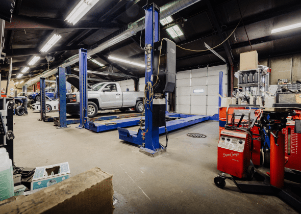 Auto repair shop with cars on hydraulic lifts, tools, and equipment, and a garage door in the background.