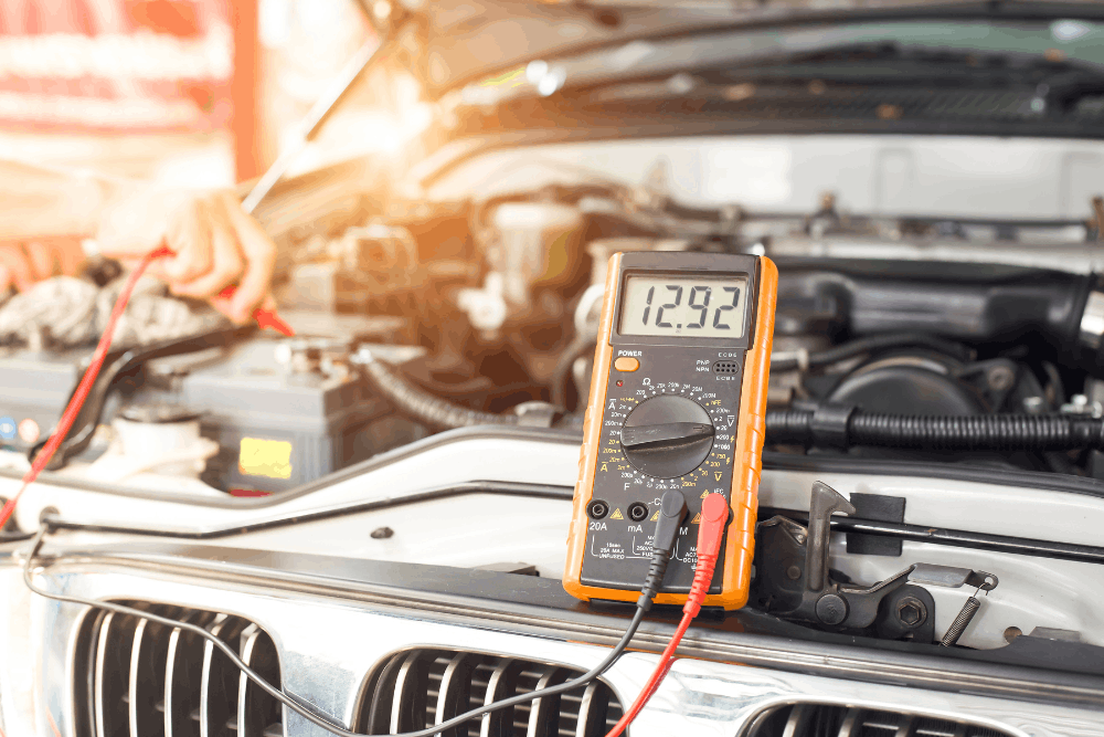 Auto electrical problems, auto repair in Chicopee, MA at E&G Automotive. Image of a multimeter testing a vehicle battery under the hood to help identify electrical problems and support reliability.